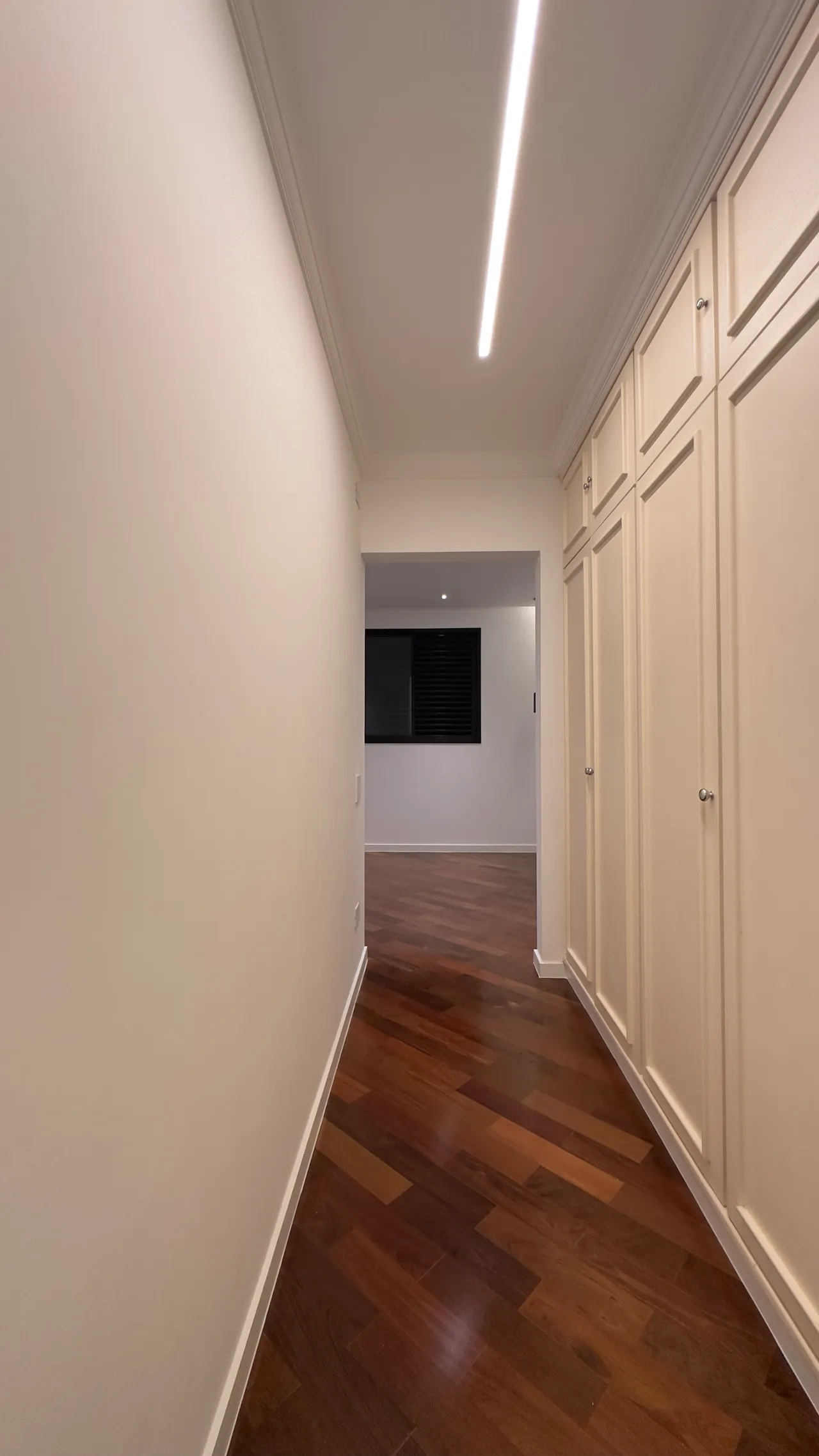 Corredor com piso de madeira e marcenaria off-white